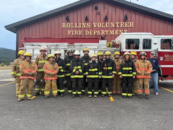 Rollins volunteer firefighters in turnout gear standing in front of the new fire station and an engine